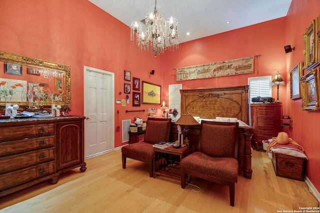 bedroom with light hardwood / wood-style floors, an inviting chandelier, and a high ceiling