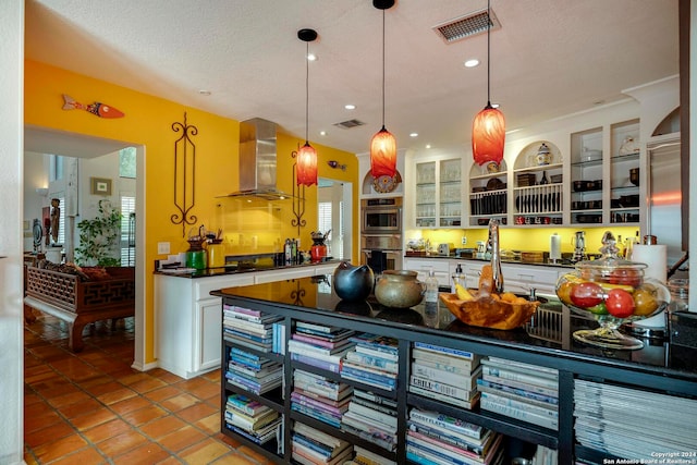 kitchen featuring stainless steel double oven, wall chimney range hood, pendant lighting, white cabinetry, and a textured ceiling