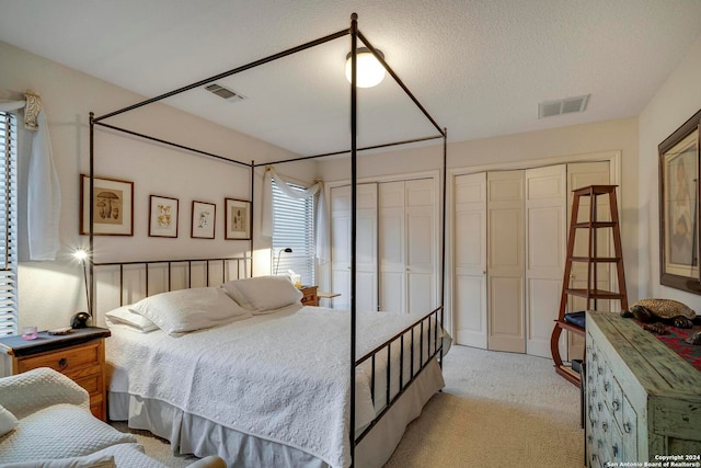 bedroom featuring multiple closets, a textured ceiling, and light colored carpet