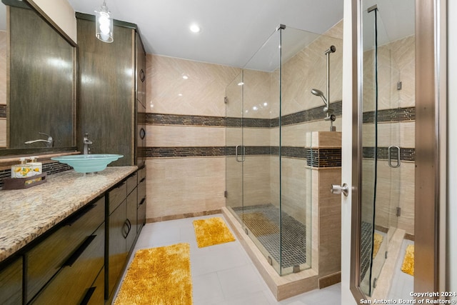 bathroom with tile walls, vanity, a shower with shower door, and tile patterned floors