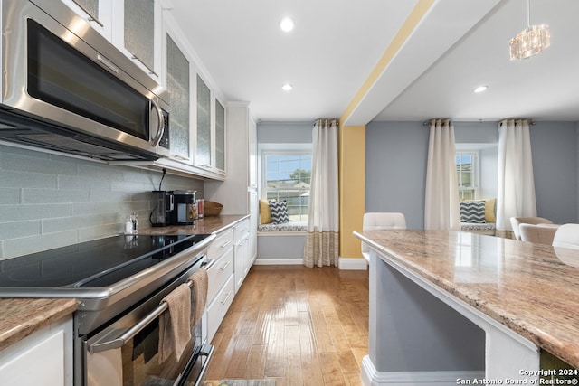 kitchen with tasteful backsplash, hanging light fixtures, stainless steel appliances, white cabinets, and light hardwood / wood-style flooring