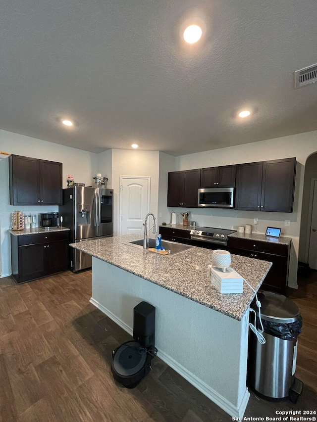 kitchen featuring sink, dark brown cabinets, dark hardwood / wood-style flooring, stainless steel appliances, and a center island with sink