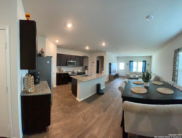 kitchen with an island with sink, light stone countertops, hardwood / wood-style flooring, sink, and stainless steel appliances