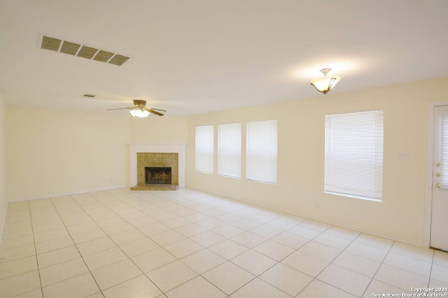 unfurnished living room featuring a tiled fireplace, light tile patterned flooring, and ceiling fan