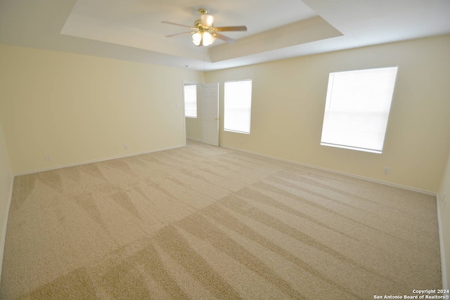 empty room with ceiling fan, a tray ceiling, and light colored carpet