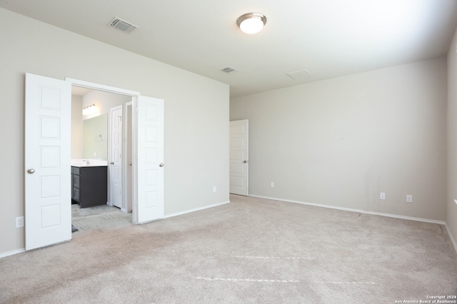 unfurnished bedroom featuring ensuite bathroom and light colored carpet