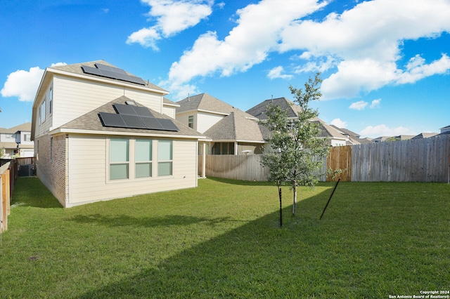 rear view of house with a yard, central AC, and solar panels