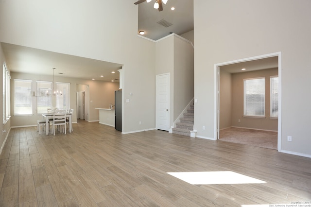 unfurnished living room with light hardwood / wood-style flooring, ceiling fan with notable chandelier, and a high ceiling