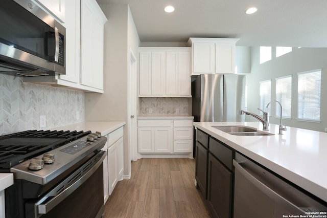 kitchen featuring sink, light wood-type flooring, backsplash, stainless steel appliances, and white cabinets