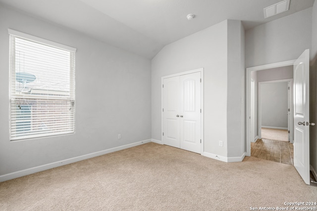 unfurnished bedroom featuring a closet, vaulted ceiling, and light colored carpet