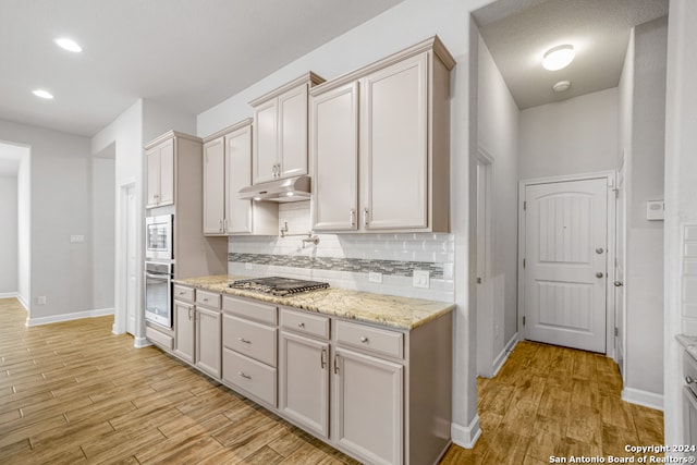 kitchen featuring backsplash, light stone counters, stainless steel appliances, and light wood-type flooring