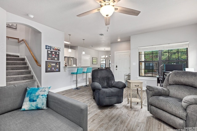 living room with light wood-type flooring and ceiling fan with notable chandelier