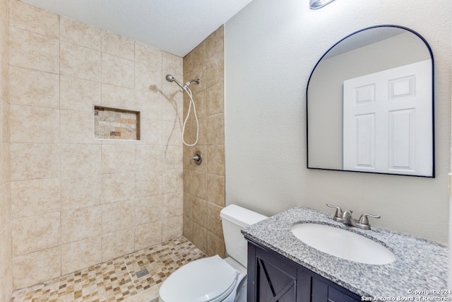 bathroom with vanity, a tile shower, a textured ceiling, and toilet