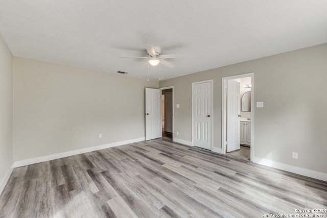 unfurnished bedroom with light hardwood / wood-style floors, a textured ceiling, connected bathroom, and ceiling fan