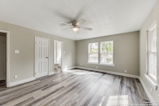 unfurnished bedroom featuring ensuite bath, a textured ceiling, light hardwood / wood-style flooring, and ceiling fan