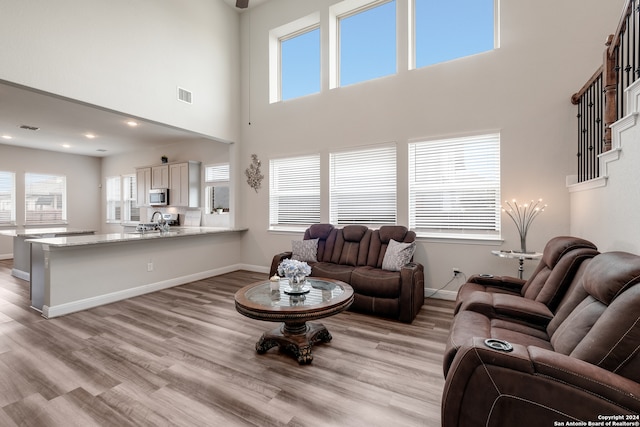 living room featuring a towering ceiling, sink, light hardwood / wood-style floors, and plenty of natural light