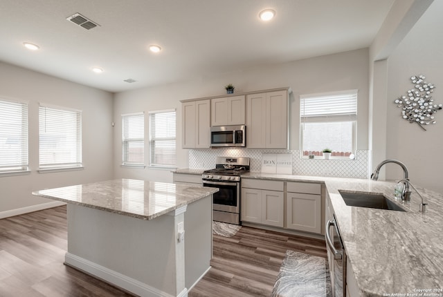 kitchen featuring decorative backsplash, light stone counters, appliances with stainless steel finishes, light wood-type flooring, and sink