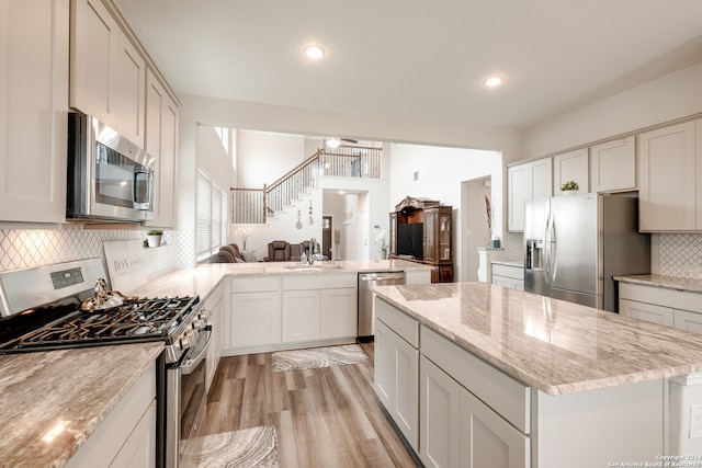 kitchen with decorative backsplash, light hardwood / wood-style flooring, kitchen peninsula, stainless steel appliances, and white cabinetry