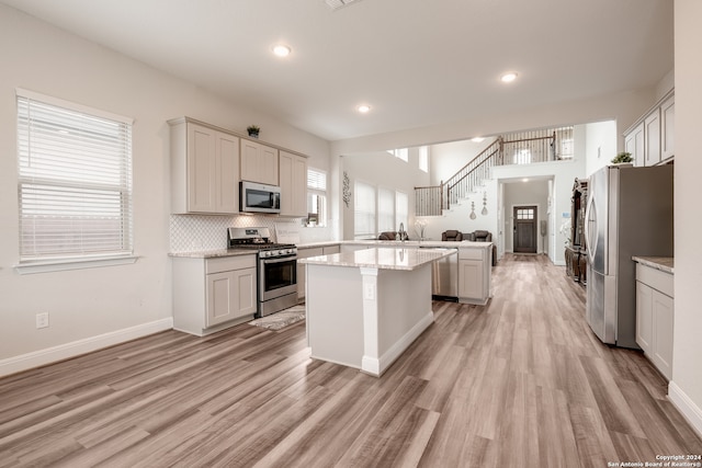 kitchen featuring appliances with stainless steel finishes, a center island, light stone counters, and light hardwood / wood-style floors