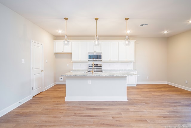 kitchen with stainless steel appliances, light stone countertops, an island with sink, and white cabinets