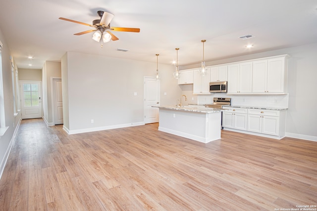 kitchen featuring white cabinets, a kitchen island with sink, light wood-type flooring, stainless steel appliances, and light stone counters