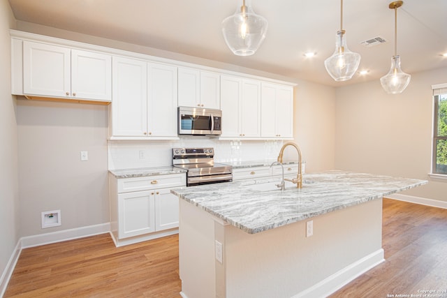 kitchen with appliances with stainless steel finishes, hanging light fixtures, a kitchen island with sink, and white cabinetry