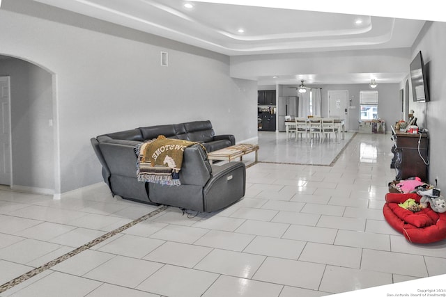 living room with light tile patterned floors, a tray ceiling, and ceiling fan