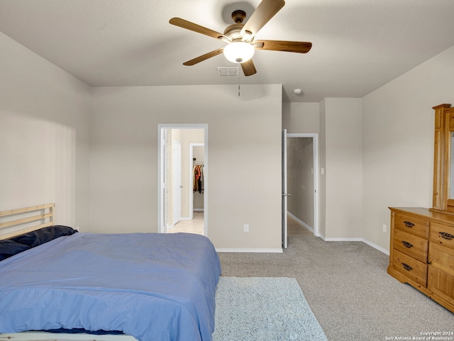 bedroom featuring ceiling fan, a walk in closet, and light colored carpet