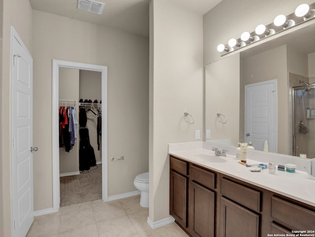 bathroom with a shower with door, vanity, toilet, and tile patterned floors