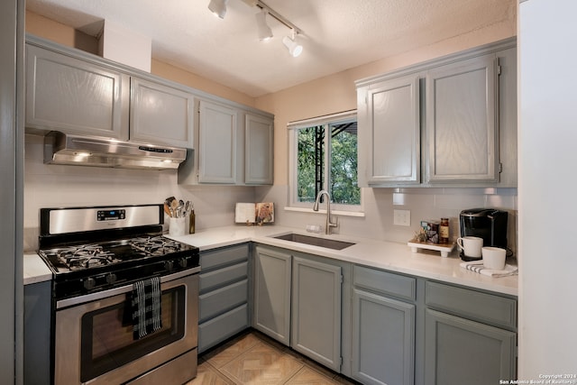 kitchen featuring stainless steel gas range oven, rail lighting, a textured ceiling, gray cabinets, and sink