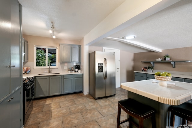 kitchen with sink, a textured ceiling, stainless steel fridge, black gas range oven, and tile counters