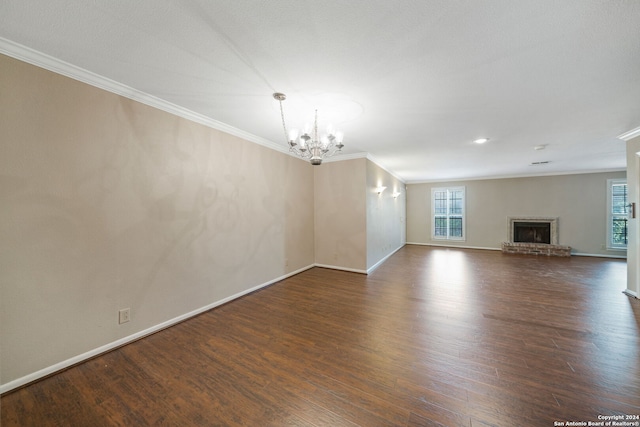 unfurnished living room with a fireplace, ornamental molding, an inviting chandelier, and dark hardwood / wood-style floors