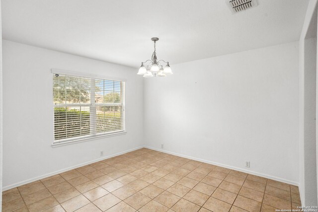 tiled spare room with a notable chandelier