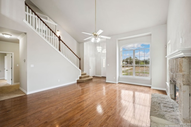 unfurnished living room with ceiling fan, a fireplace, a high ceiling, and hardwood / wood-style flooring