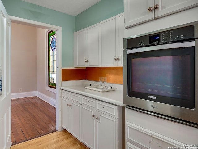 kitchen with double oven, white cabinetry, and light hardwood / wood-style floors