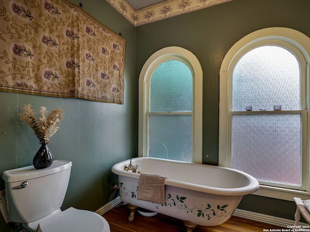 bathroom with a washtub, hardwood / wood-style floors, and toilet