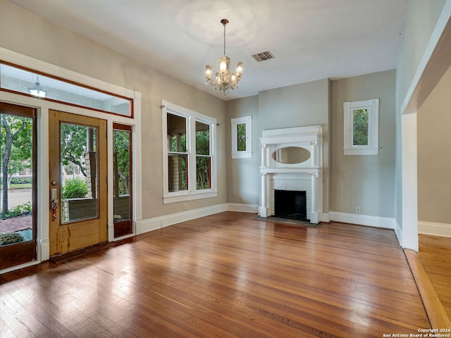 unfurnished living room with hardwood / wood-style floors, an inviting chandelier, plenty of natural light, and a brick fireplace