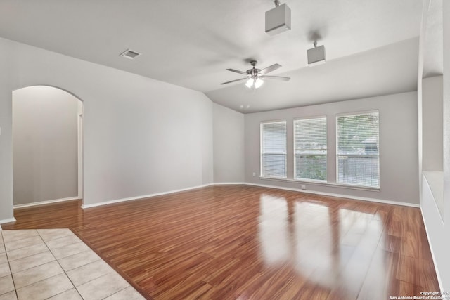 empty room featuring baseboards, arched walkways, a ceiling fan, and wood finished floors