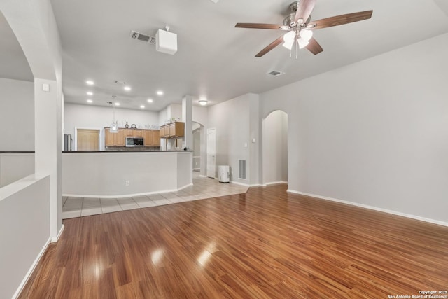 unfurnished living room with a ceiling fan, arched walkways, visible vents, and light wood-style flooring