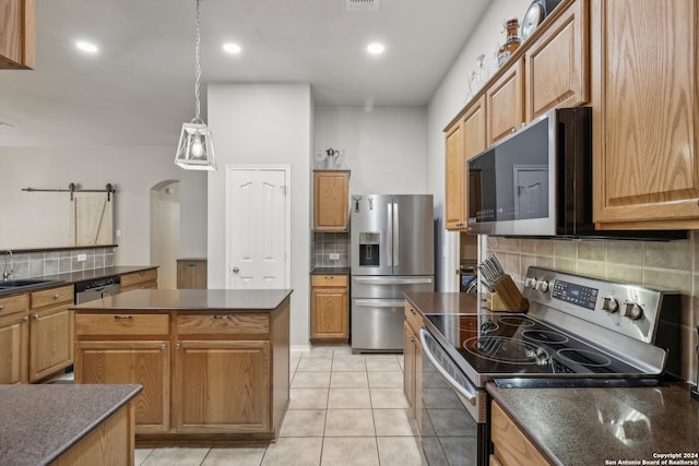 kitchen with appliances with stainless steel finishes, a barn door, a center island, decorative backsplash, and light tile patterned floors