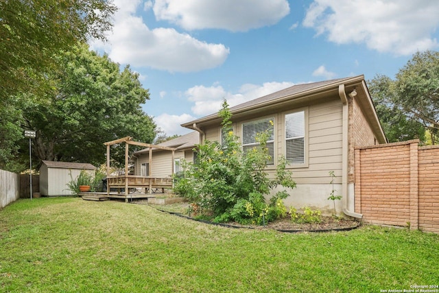 back of property featuring a wooden deck, an outbuilding, a yard, a storage unit, and fence
