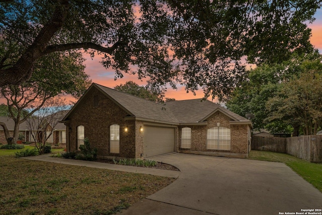 view of front of property featuring a yard, brick siding, fence, driveway, and an attached garage