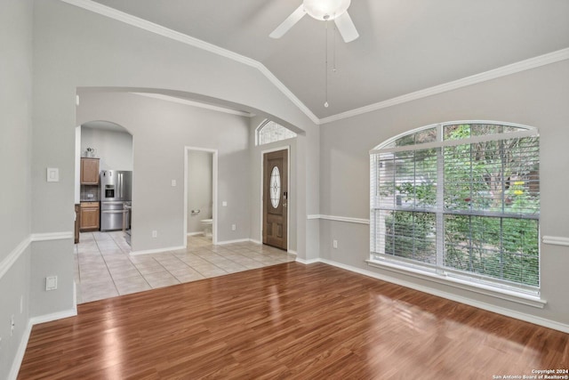 spare room featuring light wood-style floors, baseboards, arched walkways, vaulted ceiling, and a ceiling fan