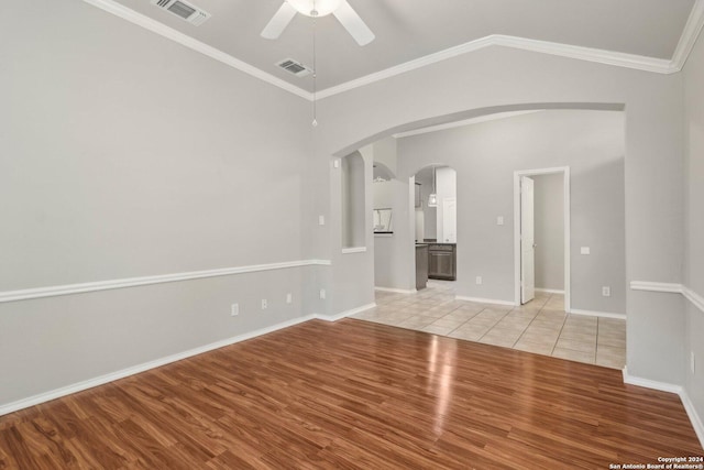 empty room with light wood-style floors, visible vents, a ceiling fan, and arched walkways