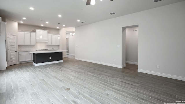 kitchen with an island with sink, white cabinets, pendant lighting, ceiling fan with notable chandelier, and backsplash