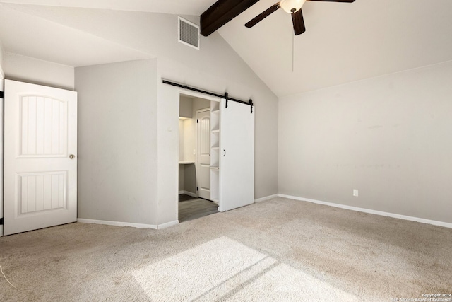 unfurnished bedroom with carpet, ceiling fan, a barn door, vaulted ceiling with beams, and ensuite bathroom