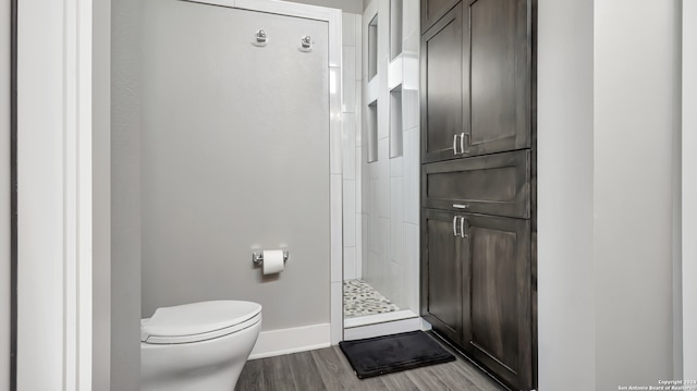 bathroom featuring toilet, wood-type flooring, and a tile shower