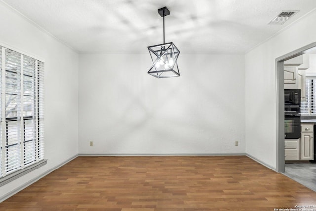 unfurnished dining area featuring a wealth of natural light, wood-type flooring, and a notable chandelier