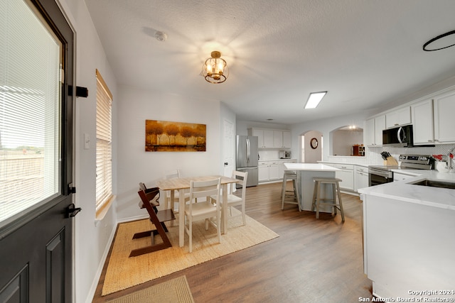 kitchen featuring kitchen peninsula, white cabinets, hardwood / wood-style floors, appliances with stainless steel finishes, and a kitchen breakfast bar