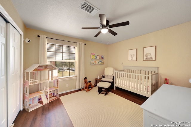 bedroom with ceiling fan, dark hardwood / wood-style flooring, a nursery area, a textured ceiling, and a closet